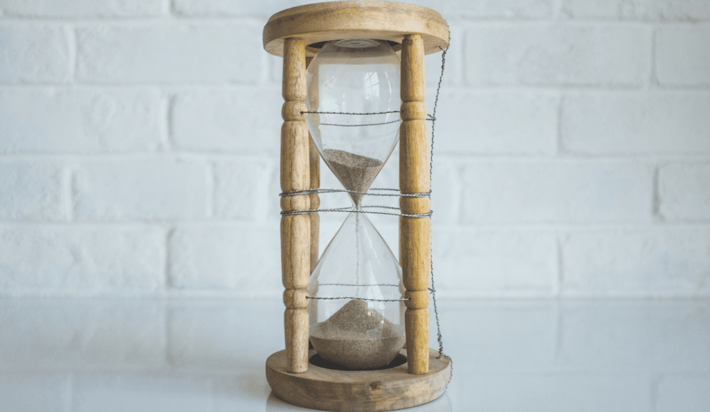 Wooden hourglass against white brick wall.