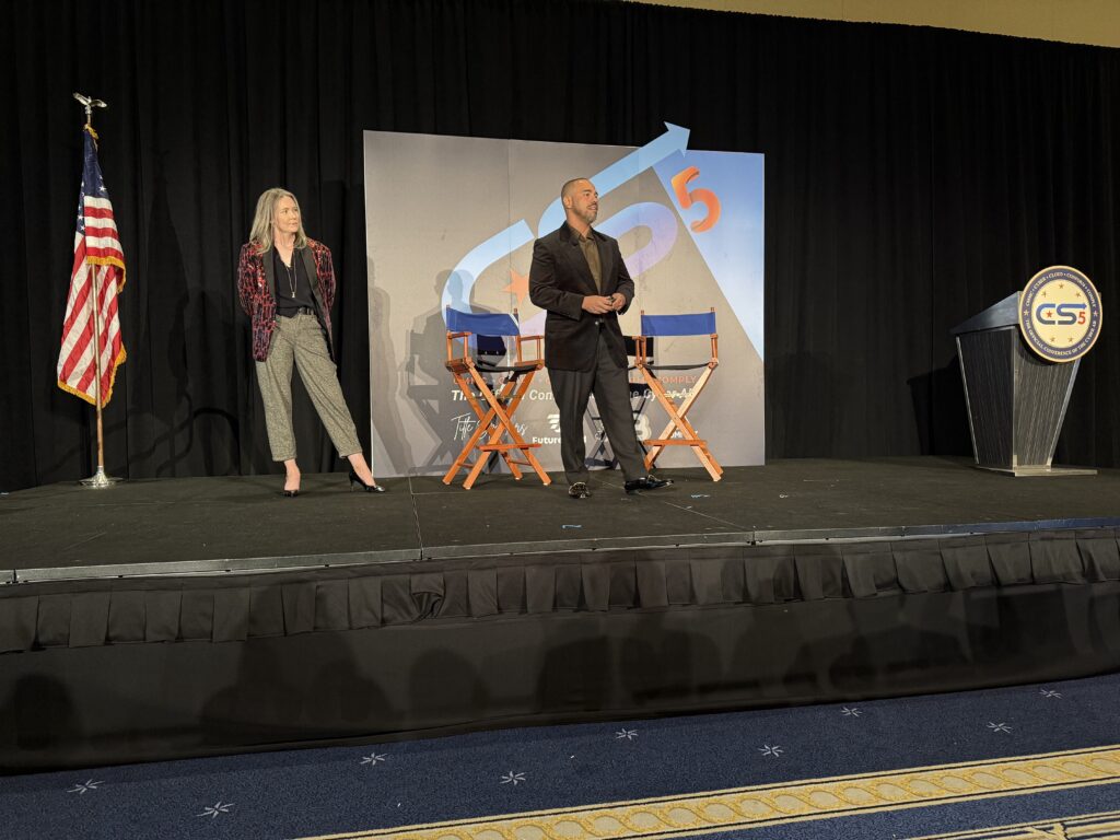 Two people speaking on stage with chairs.