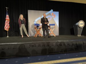 Two people speaking on stage with chairs.